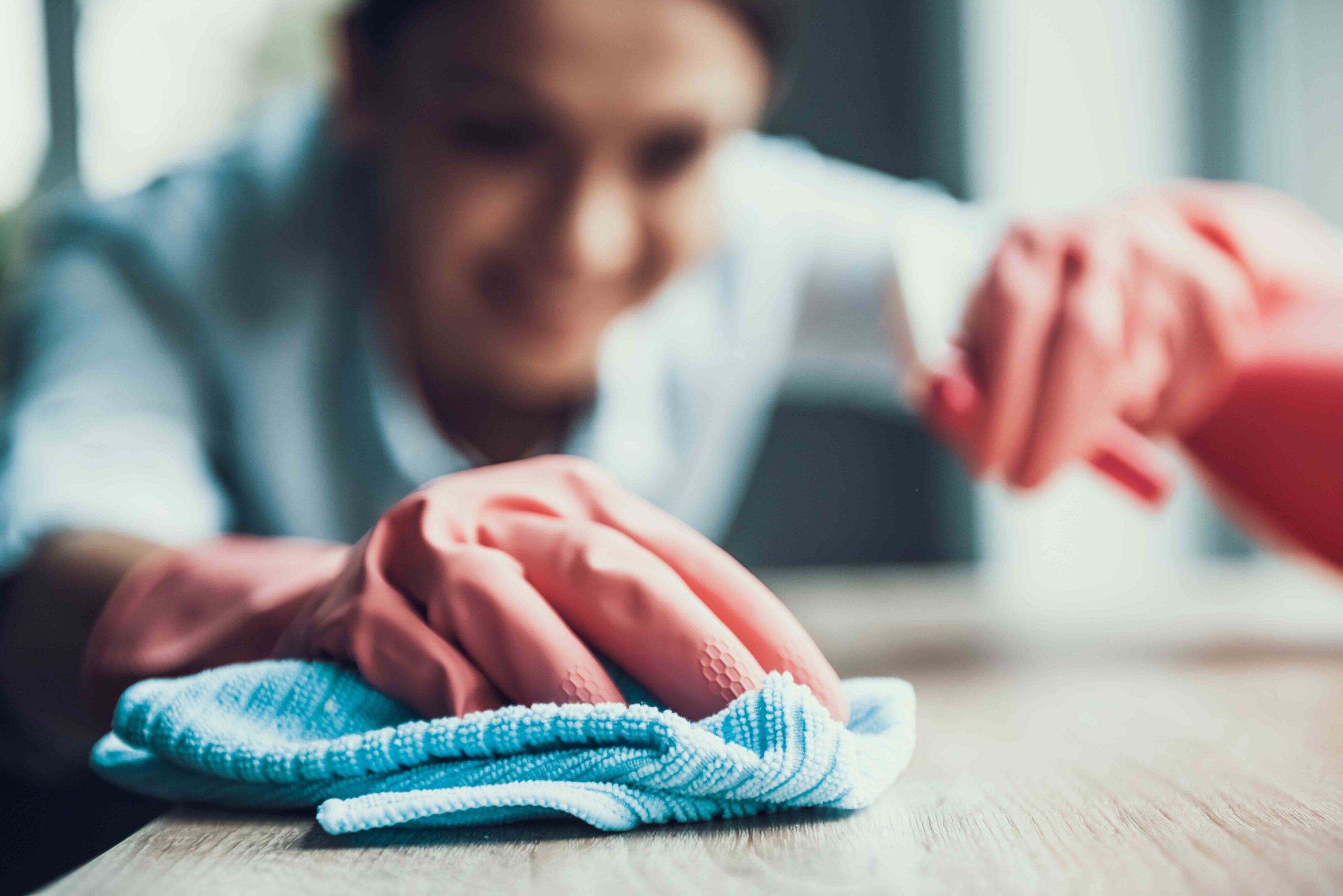 Young Smiling Woman in Gloves Cleaning House. Closeup of Happy Beautiful Girl wearing Protective Gloves Cleaning Desk by spraying Cleaning Products and wiping with Sponge. Woman Cleaning Apartment