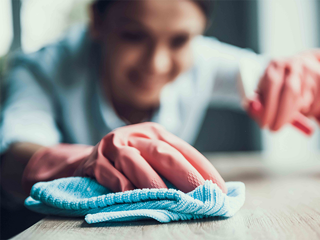 Young Smiling Woman in Gloves Cleaning House. Closeup of Happy Beautiful Girl wearing Protective Gloves Cleaning Desk by spraying Cleaning Products and wiping with Sponge. Woman Cleaning Apartment